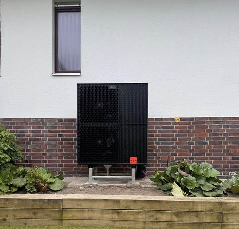 Wärmepumpen-Außengerät an der Hauswand, eingebettet ins Beet